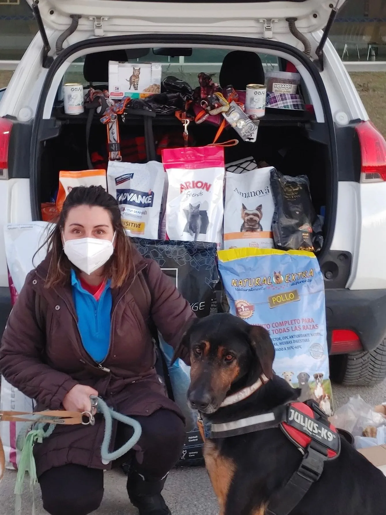 Una voluntaria y un perro junto a un coche cargado con alimento y material para los animales.